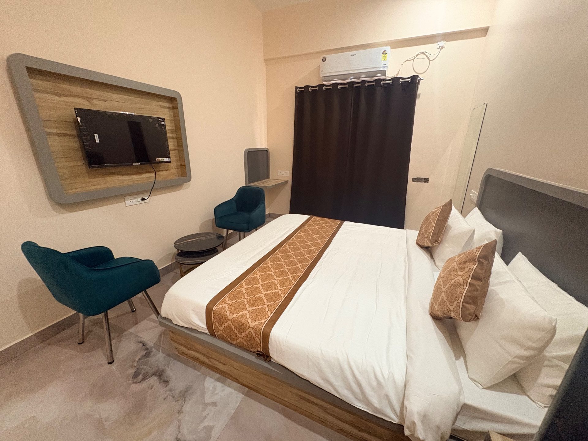 Deluxe Room at City Comfort Hotel — a made-up bed with teal armchairs and a wood-framed TV wall
